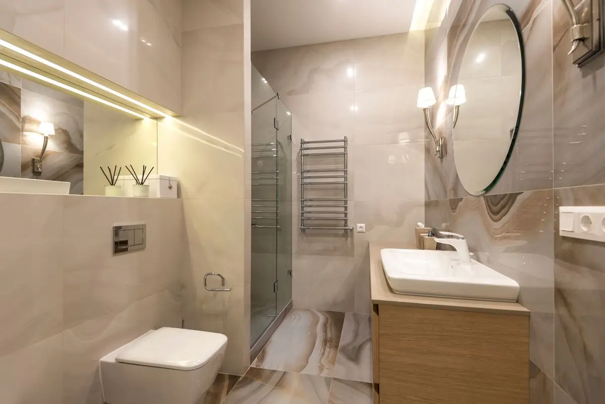 Baño con revestimiento de mármol, espejo grande y lavamanos